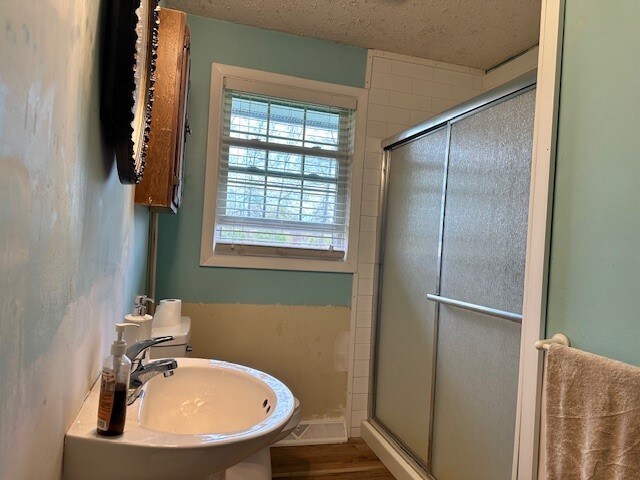 full bathroom with wood finished floors, a sink, a textured ceiling, and a stall shower