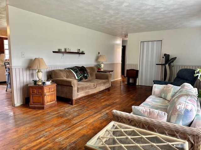 living area featuring a textured ceiling, a wainscoted wall, and hardwood / wood-style flooring