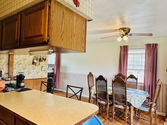 kitchen with light countertops, ceiling fan, light wood-type flooring, and a wainscoted wall
