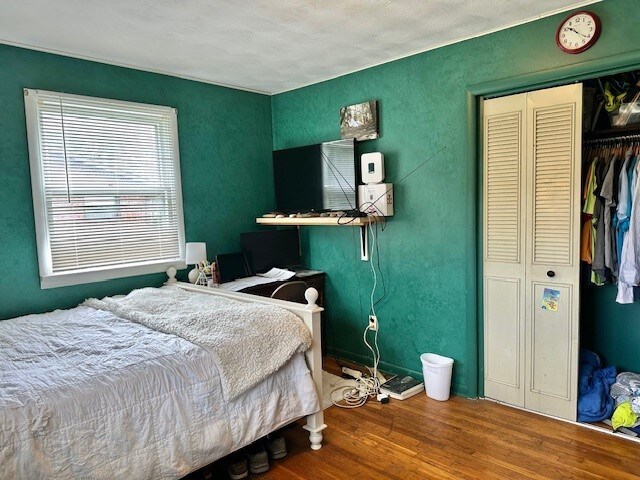 bedroom featuring a closet, baseboards, a textured wall, and wood finished floors