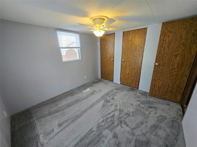 unfurnished bedroom with ceiling fan, light colored carpet, and multiple closets