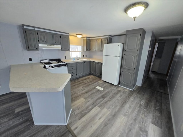 kitchen with kitchen peninsula, gray cabinetry, dark hardwood / wood-style floors, white appliances, and sink