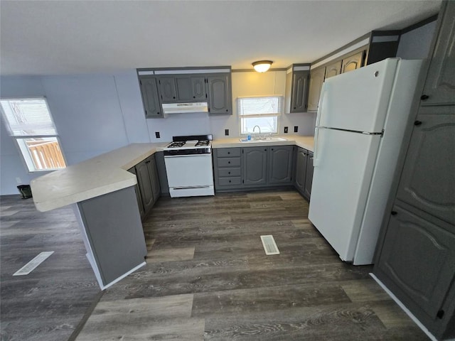 kitchen with dark wood-type flooring, white appliances, kitchen peninsula, and a healthy amount of sunlight