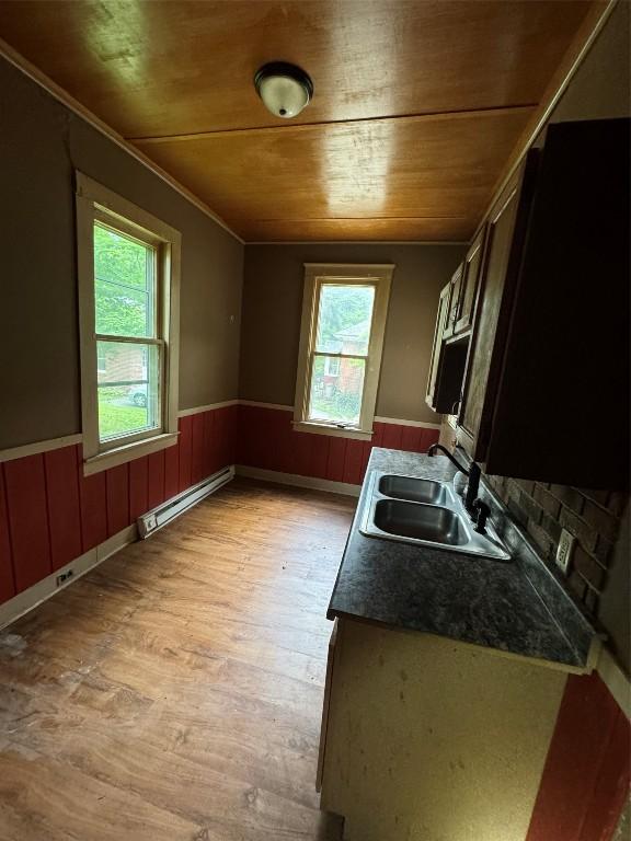 kitchen featuring light wood-type flooring, baseboard heating, wooden walls, sink, and wooden ceiling