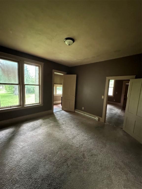 unfurnished bedroom featuring dark carpet and a baseboard heating unit