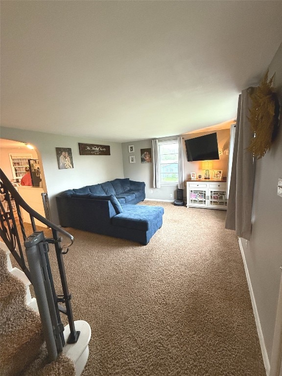 carpeted living area with stairs, arched walkways, and baseboards