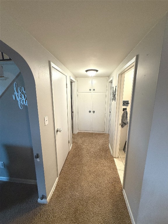 hallway with arched walkways, baseboards, and light colored carpet
