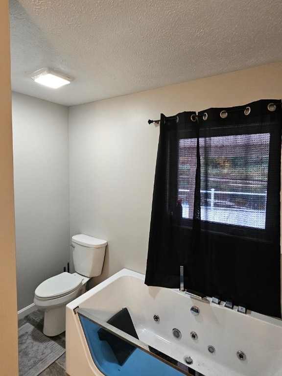 bathroom featuring a bath, a textured ceiling, and toilet