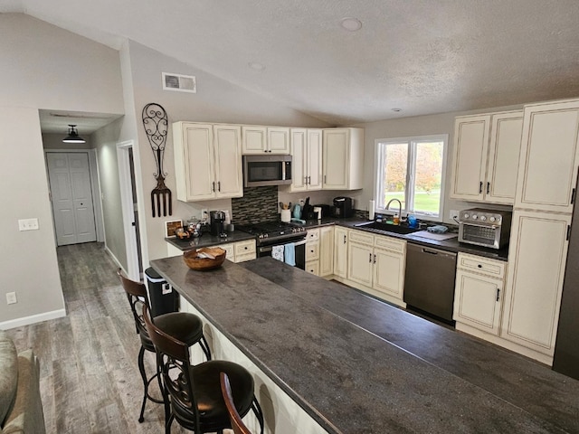 kitchen featuring sink, tasteful backsplash, vaulted ceiling, appliances with stainless steel finishes, and hardwood / wood-style flooring