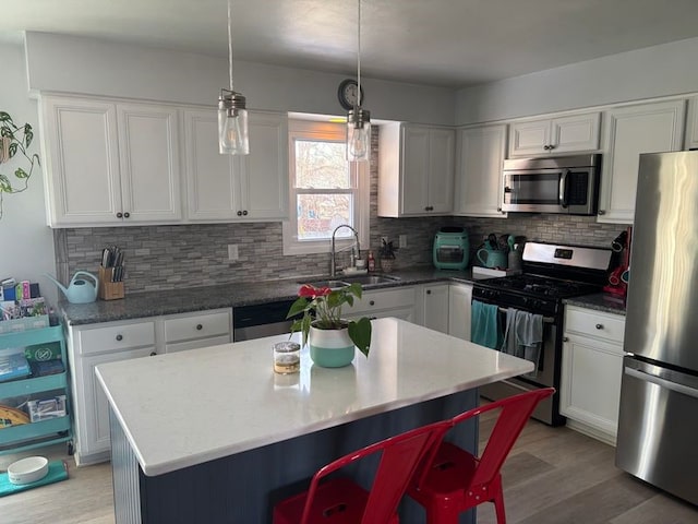 kitchen with pendant lighting, sink, appliances with stainless steel finishes, white cabinetry, and a kitchen island