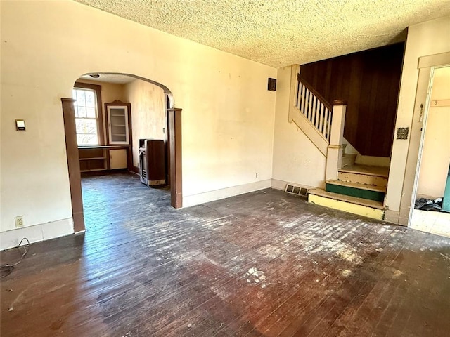 unfurnished living room with stairway, hardwood / wood-style floors, a textured ceiling, arched walkways, and visible vents