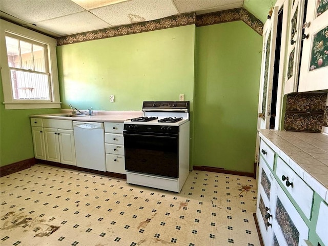 kitchen featuring range with gas stovetop, tile counters, white dishwasher, a sink, and a drop ceiling