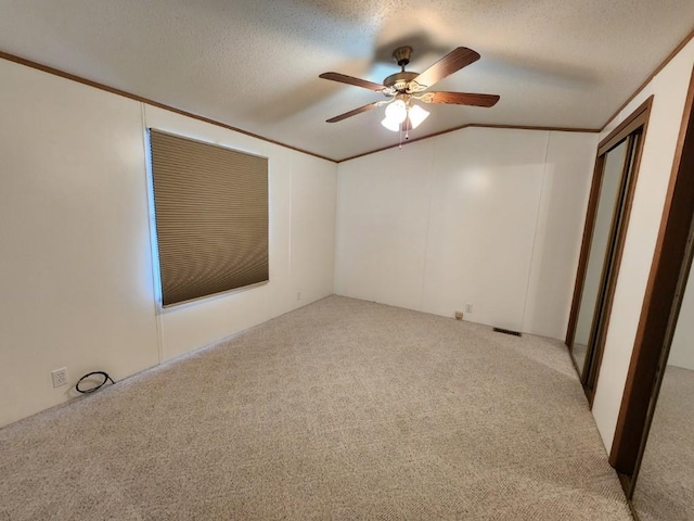 carpeted empty room with ceiling fan, vaulted ceiling, ornamental molding, and a textured ceiling