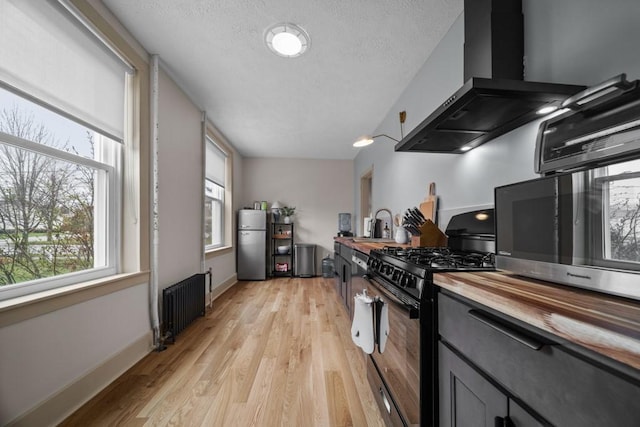 51-55 E Main St, North East, PA 16428 - kitchen with black range with gas cooktop, radiator heating unit, wall chimney range hood, freestanding refrigerator, and butcher block countertops