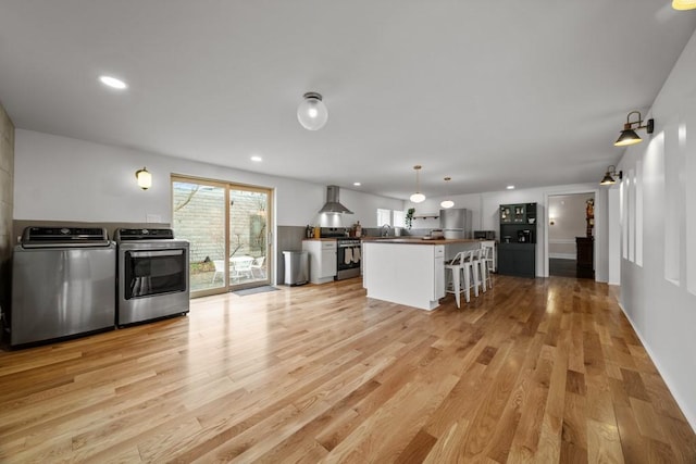 51-55 E Main St, North East, PA 16428 - kitchen with stainless steel appliances, wall chimney exhaust hood, washing machine and dryer, light wood-style floors, and a kitchen bar