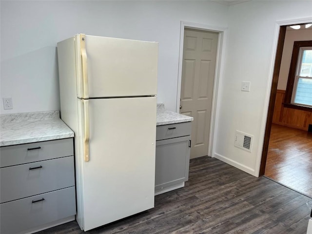 kitchen featuring white refrigerator, dark hardwood / wood-style floors, gray cabinetry, and wooden walls