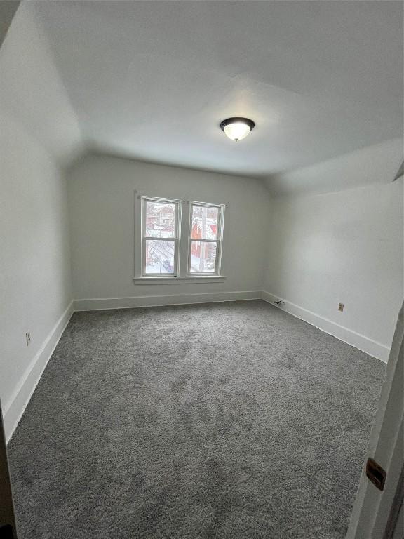 additional living space featuring lofted ceiling and dark carpet