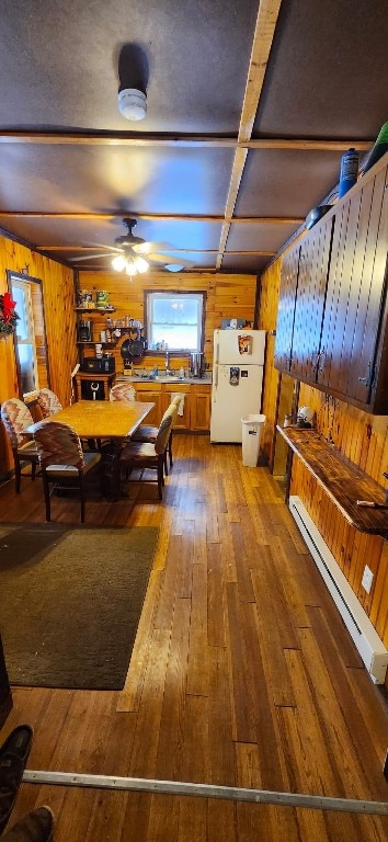 dining area featuring hardwood / wood-style floors, wood walls, ceiling fan, and baseboard heating