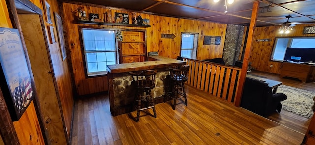 bar with hardwood / wood-style floors, ceiling fan, and wood walls