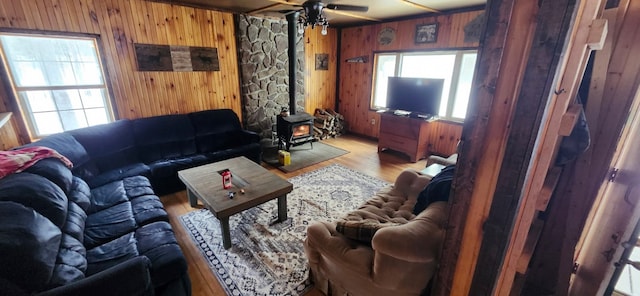 living room with light wood-type flooring, a wood stove, wood walls, and a healthy amount of sunlight