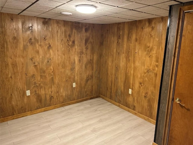 empty room featuring a paneled ceiling, wooden walls, and light hardwood / wood-style flooring