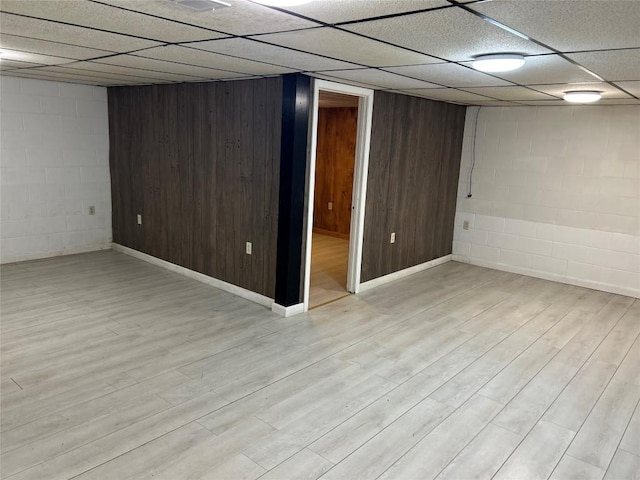 basement featuring a paneled ceiling and wooden walls