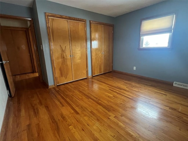 unfurnished bedroom featuring multiple closets and light hardwood / wood-style floors