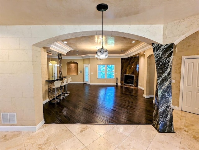 entryway featuring a raised ceiling, ornamental molding, a fireplace, wood-type flooring, and a chandelier