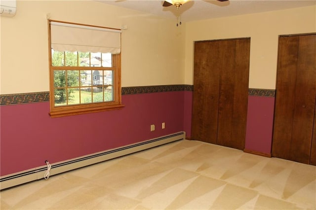 unfurnished bedroom with a baseboard heating unit, an AC wall unit, carpet, a ceiling fan, and two closets