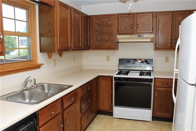 kitchen featuring under cabinet range hood, light countertops, a sink, freestanding refrigerator, and gas range
