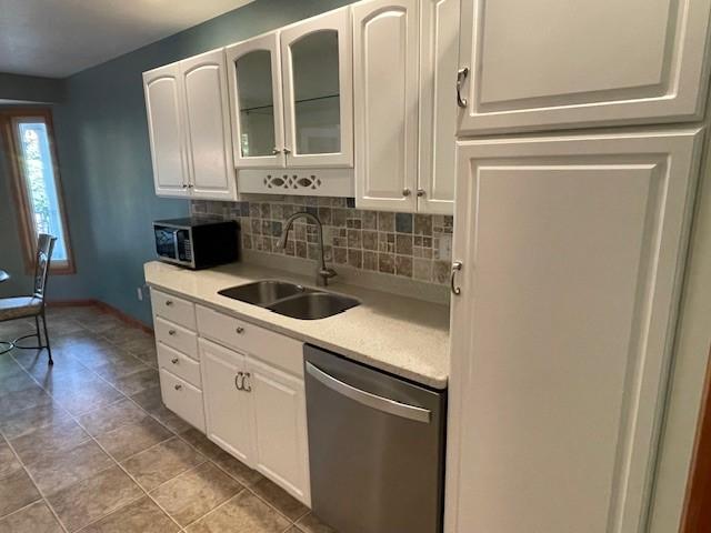 kitchen with stainless steel dishwasher, white cabinets, sink, and tasteful backsplash