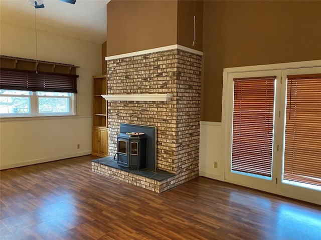 unfurnished living room with a wood stove, ceiling fan, and dark hardwood / wood-style flooring