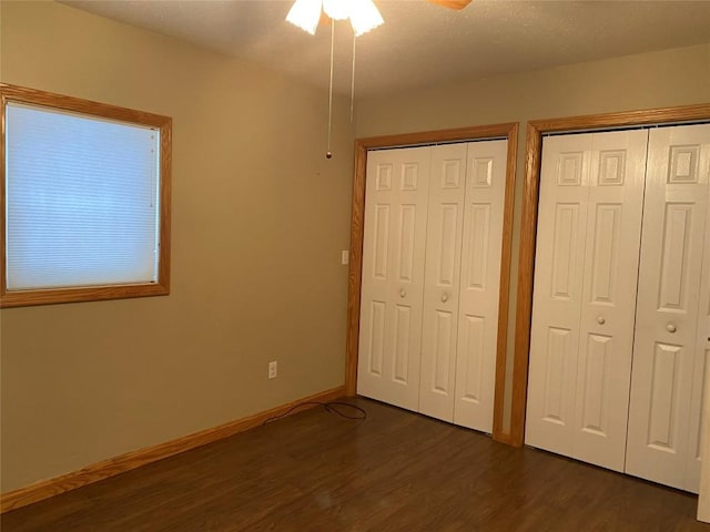 unfurnished bedroom featuring ceiling fan, dark wood-type flooring, and two closets