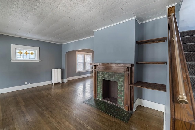 unfurnished living room featuring crown molding, a brick fireplace, dark wood-type flooring, and radiator heating unit