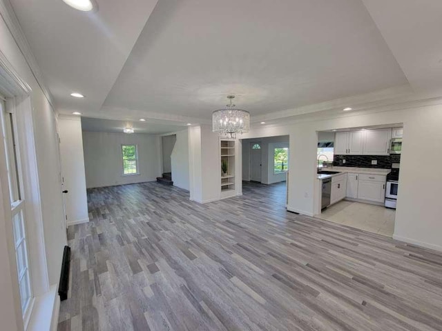 unfurnished living room with a tray ceiling, light hardwood / wood-style flooring, a notable chandelier, and sink