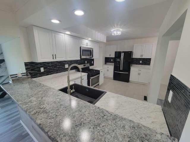 kitchen with kitchen peninsula, backsplash, light stone counters, stainless steel appliances, and white cabinets