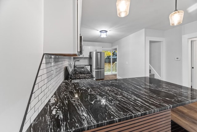 kitchen featuring kitchen peninsula, backsplash, decorative light fixtures, white cabinets, and stainless steel refrigerator