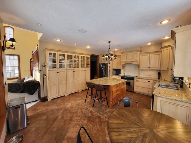 kitchen with a notable chandelier, cream cabinetry, a sink, stainless steel appliances, and decorative backsplash