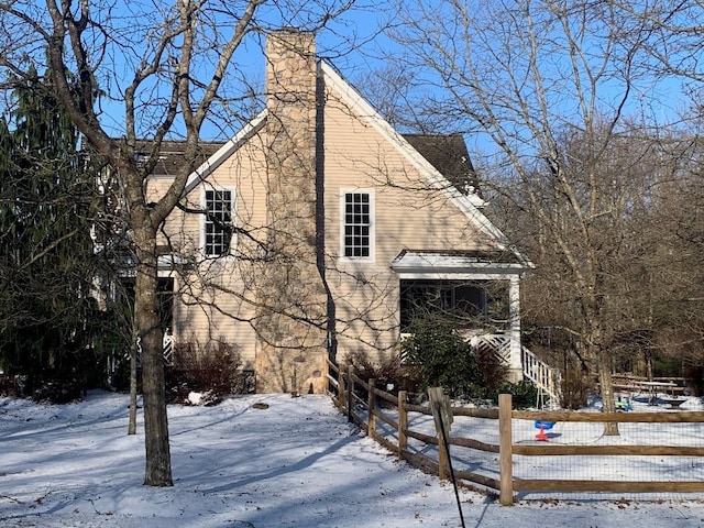 view of snowy exterior featuring a chimney and fence