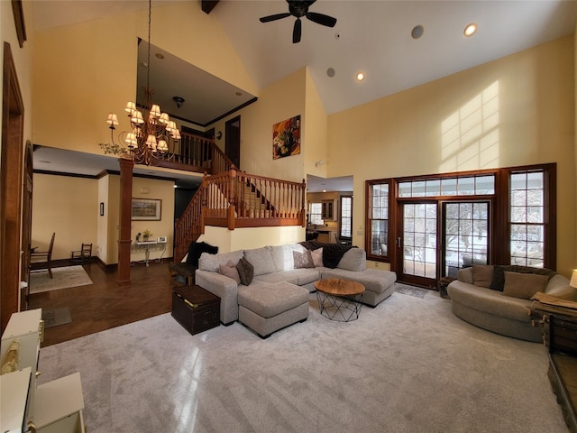 living area featuring stairs, decorative columns, ceiling fan with notable chandelier, and high vaulted ceiling