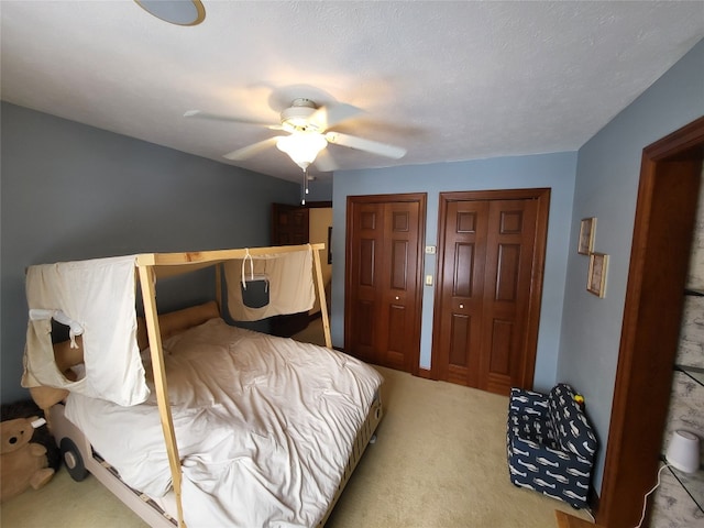 bedroom featuring light carpet, two closets, and ceiling fan