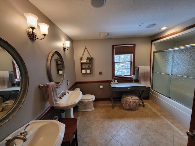 full bathroom featuring tile patterned floors, toilet, a sink, a textured ceiling, and bath / shower combo with glass door