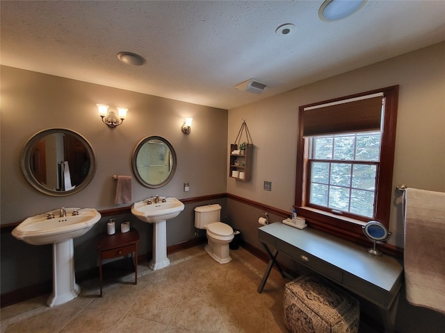 bathroom with a textured ceiling, toilet, visible vents, and a sink