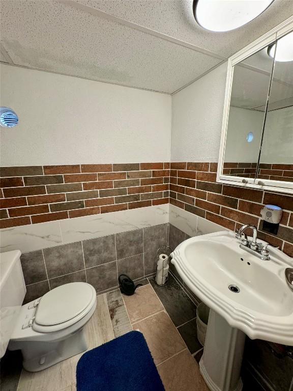 bathroom with tile patterned flooring, toilet, tile walls, and a textured ceiling