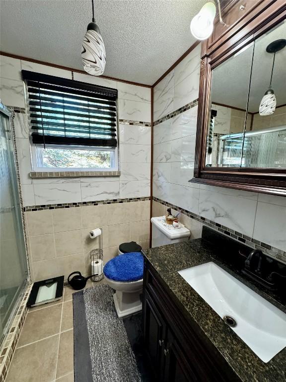 bathroom featuring vanity, tile patterned flooring, a textured ceiling, walk in shower, and tile walls