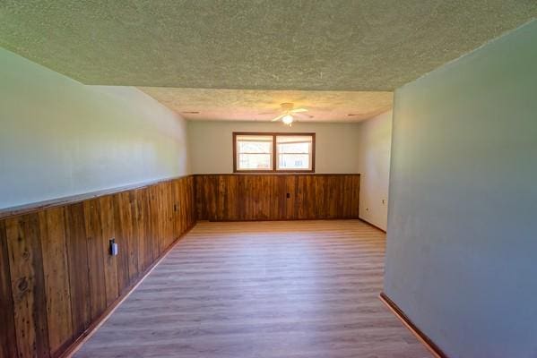 unfurnished room featuring a textured ceiling, wood walls, wainscoting, and wood finished floors