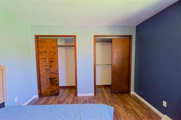 unfurnished bedroom featuring baseboards, multiple closets, and wood finished floors