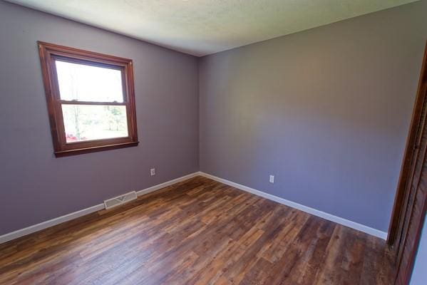 spare room featuring baseboards, dark wood-style floors, and visible vents
