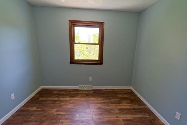 empty room with baseboards, visible vents, and wood finished floors