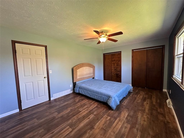unfurnished bedroom with baseboards, a textured ceiling, wood finished floors, and two closets